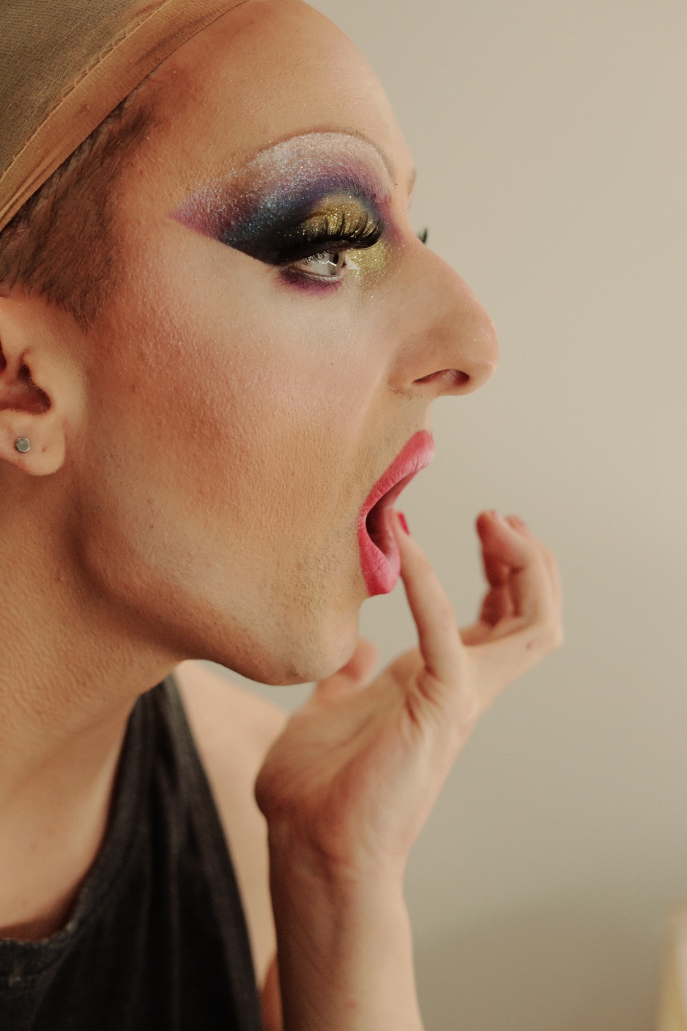 Zbliżenie na portret osoby w makijażu drag Michała Sienkiewicza aka Babsi Bonèr z dramatycznymi fioletowo-złotymi cieniami do powiek, błyszczącymi ustami 